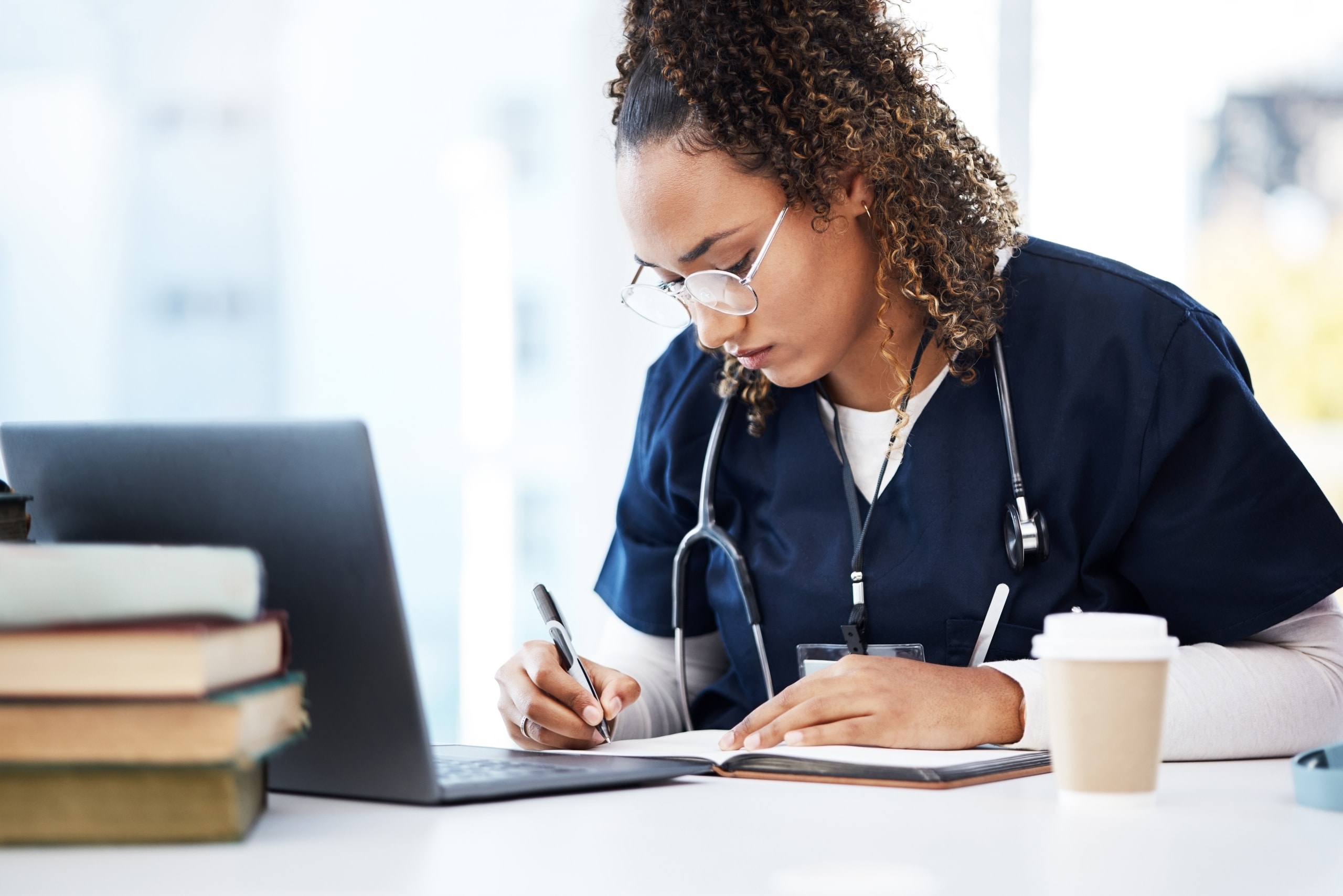 African-American nurse using a laptop and textbooks to study